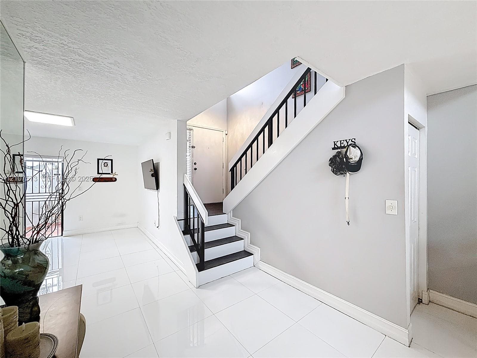 Staircase featuring black-painted treads, white risers, and a metal balustrade, complemented by polished white tile flooring
