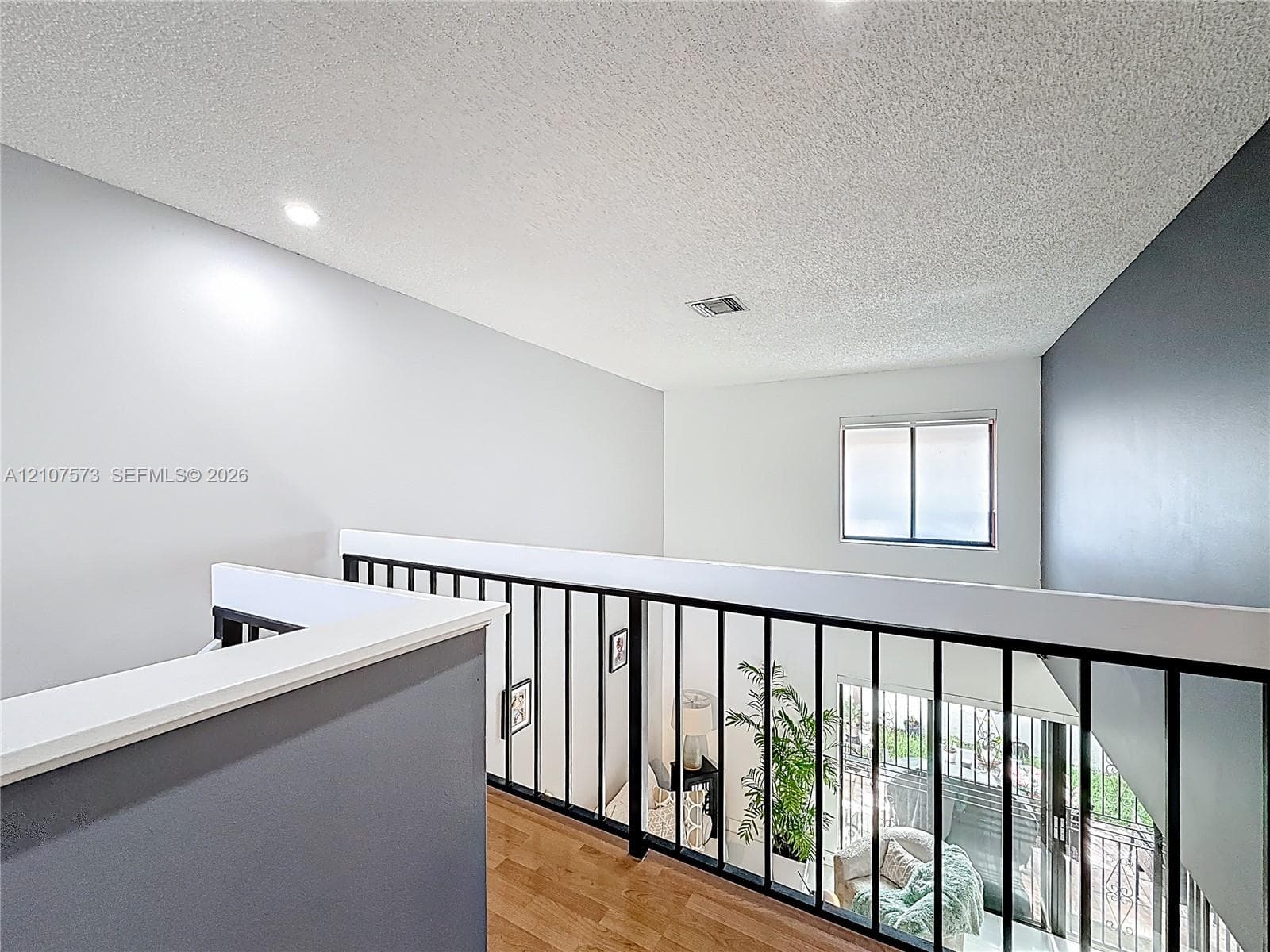 Interior balcony featuring wood-finish flooring, matte black metal railings, recessed lighting, and high ceilings