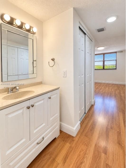 White vanity with a solid-surface countertop and integrated sink, framed wall-mounted mirror, four-bulb vanity lighting, bi-fold closet doors, and wood-finish flooring