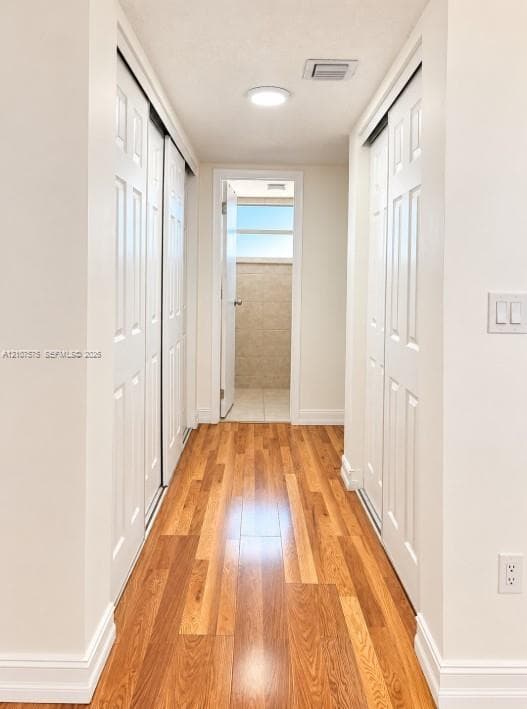 Hallway featuring wood-finish flooring, dual sets of white paneled sliding closet doors, and flush-mount lighting