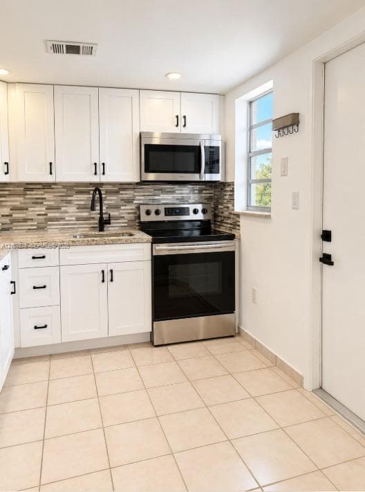 Kitchen featuring white cabinetry, stone-finish countertops, stainless steel appliances, multi-toned decorative backsplash, and ceramic tile flooring
