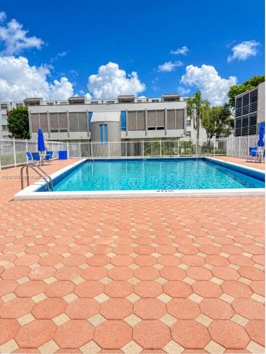 Rectangular swimming pool featuring a geometric paver deck and white perimeter fencing