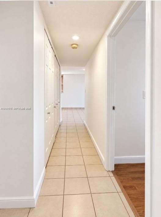 Hallway featuring neutral-toned tile flooring, recessed lighting, and double-door closets