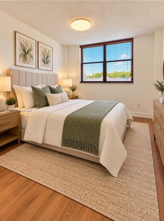 Bedroom featuring wood-finish flooring, a large window with horizontal blinds, and a neutral-toned ceiling-mounted light fixture