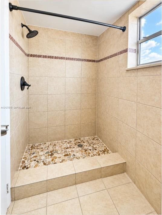 Walk-in shower featuring pebble stone floor tiling, neutral wall tile with decorative accent border, and matte black shower fixtures
