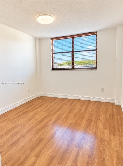 Interior space featuring wood-finish flooring, white walls, flush-mount ceiling lighting, and a window with wood-tone horizontal blinds