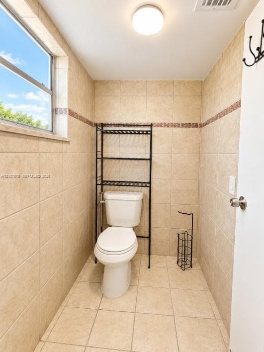 Ceramic tile walls and flooring featuring a decorative accent border, single-hung window, and flush-mount lighting