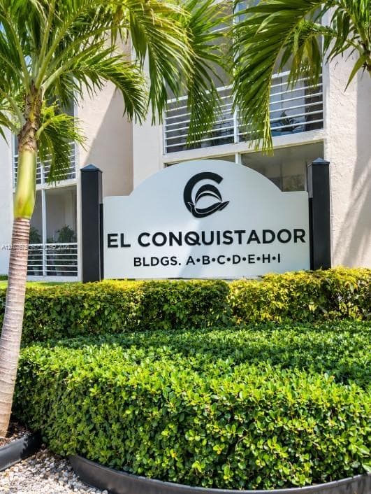 El Conquistador signage featuring structural metal framing, manicured shrubbery, and mature palm trees