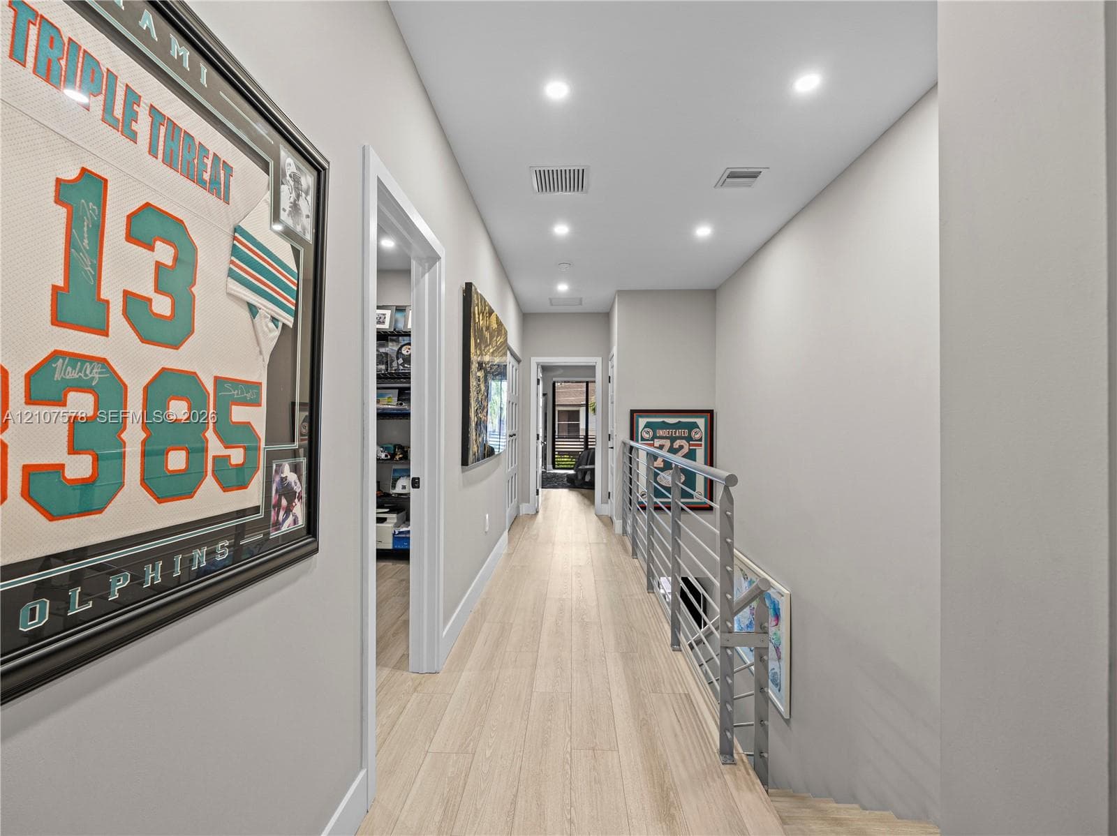 Hallway featuring light-toned wood-finish flooring, recessed ceiling lighting, and a metal horizontal-bar railing