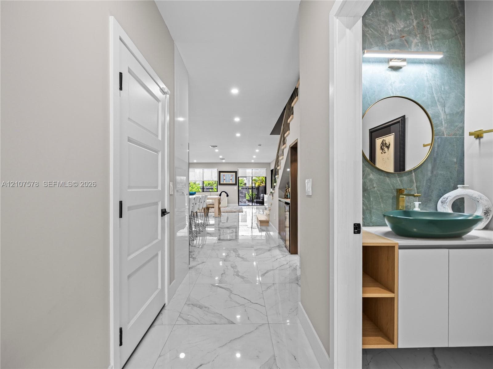 Hallway featuring large-format tile flooring and recessed lighting, with a powder room showcasing a green stone slab backsplash, vessel sink, and built-in vanity cabinet