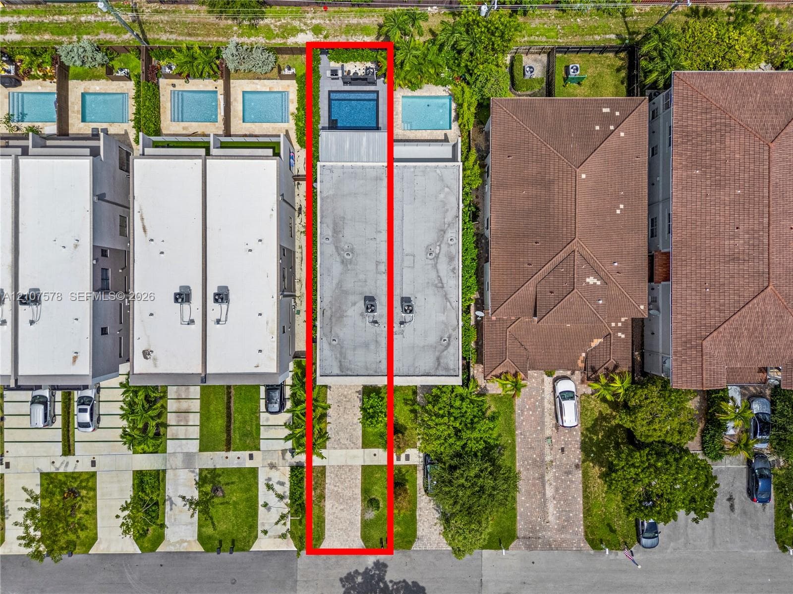 Aerial perspective featuring a paved driveway, a flat roofline, and a rear swimming pool with a stone-surfaced patio