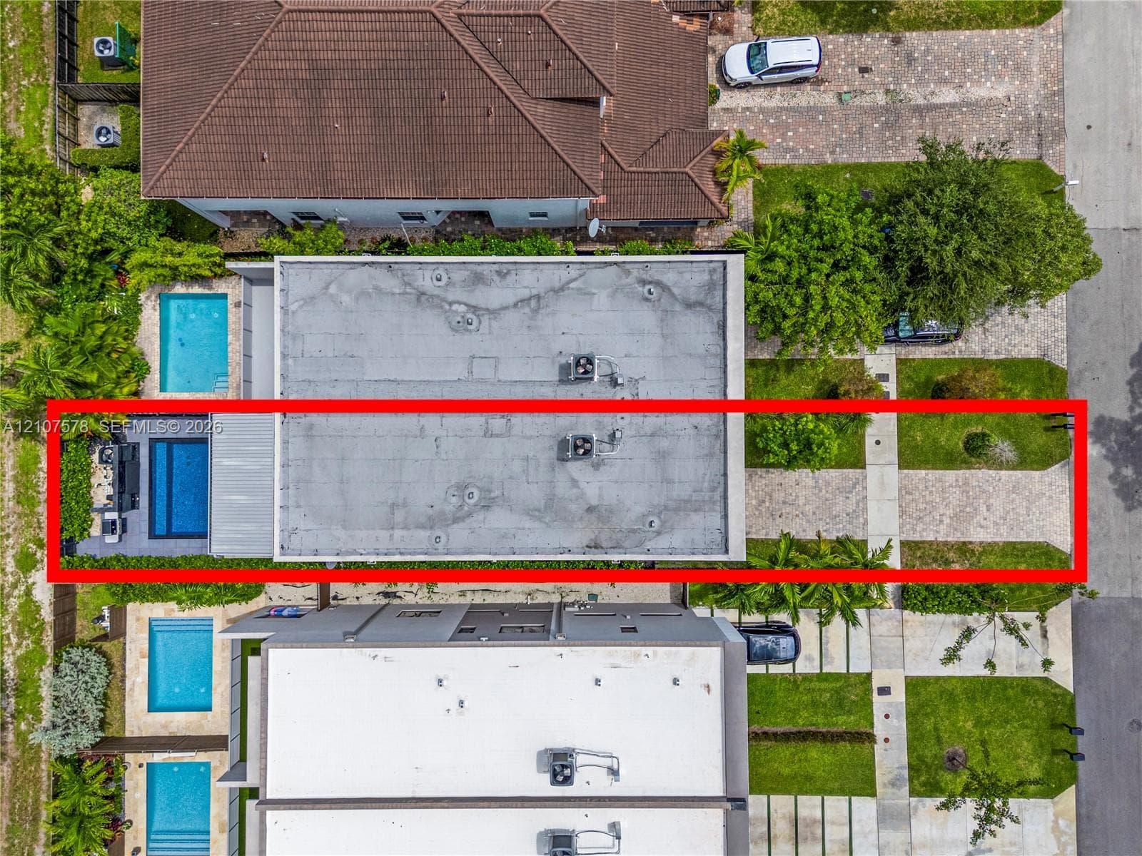 Aerial view of residential property featuring a rectangular swimming pool, concrete hardscaping, paved driveway, and established perimeter landscaping