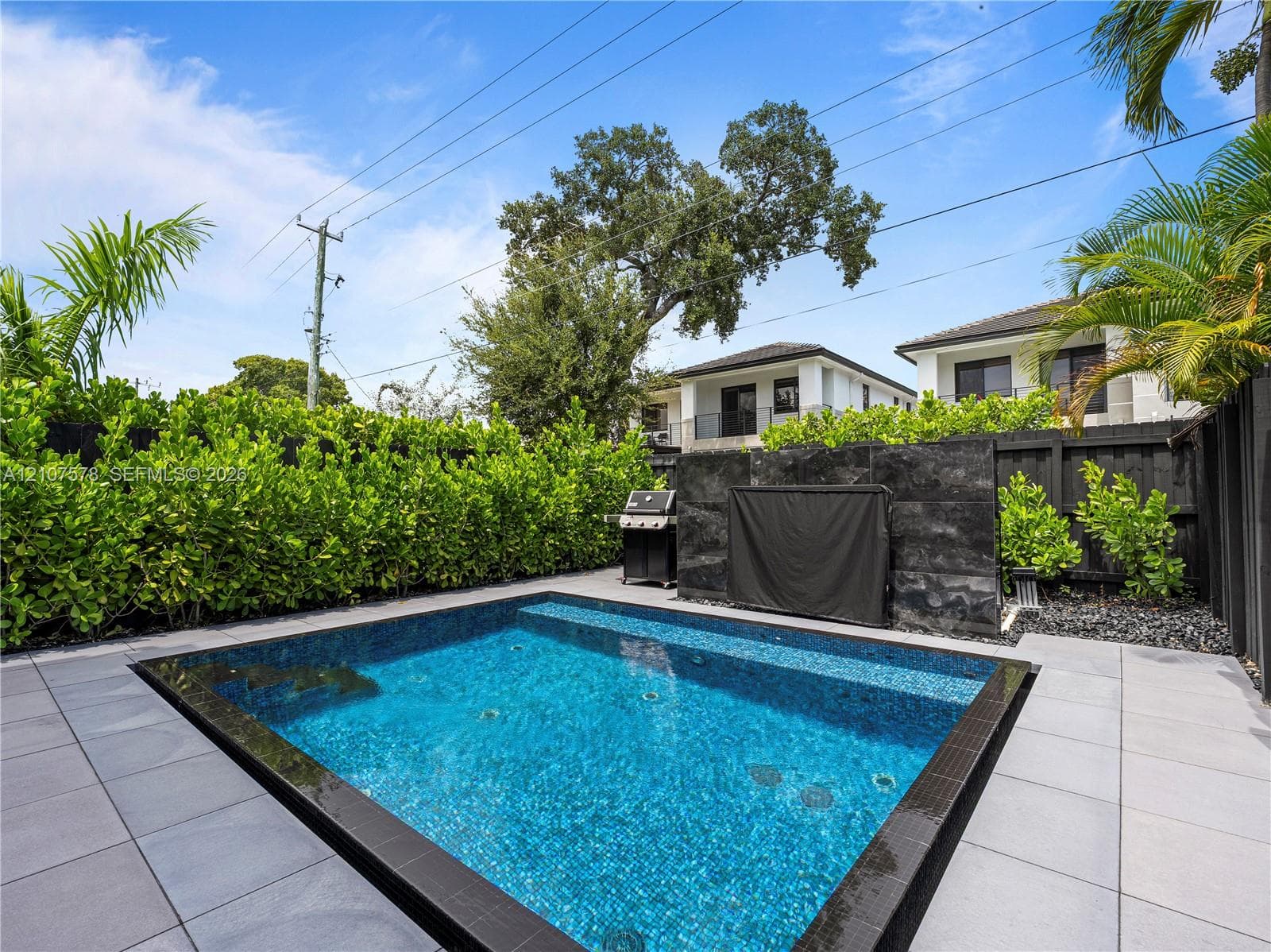 Private courtyard featuring a plunge pool with mosaic tile finish, large-format concrete paver decking, and a structured stone-veneer accent wall enclosed by perimeter hedging