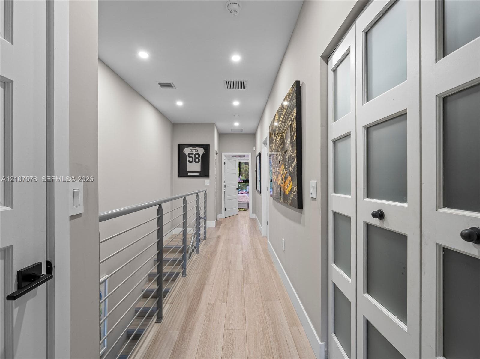Hallway featuring wood-finish flooring, recessed lighting, double doors with frosted glass panels, and a metal horizontal-bar railing