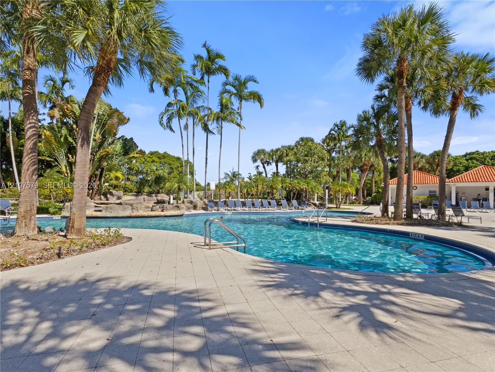 Free-form swimming pool featuring rock-wall water features, expansive paver decking, and surrounding mature palm trees