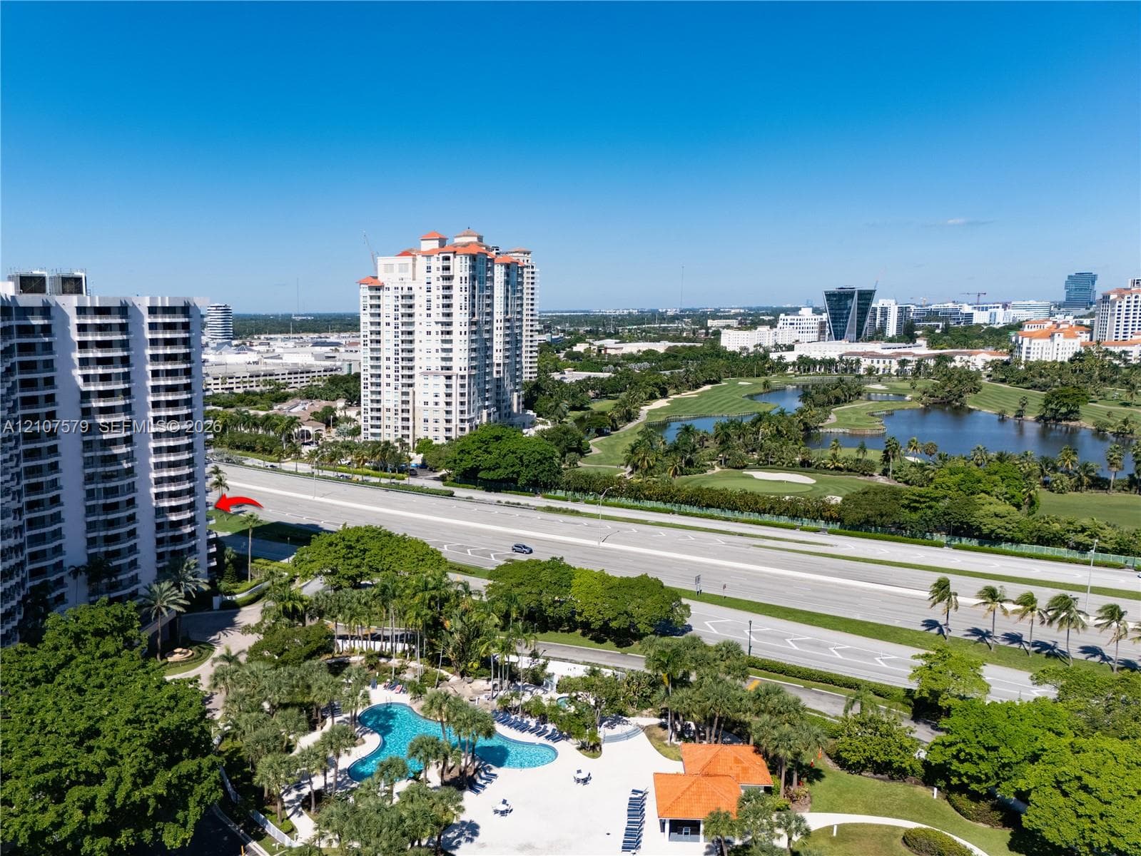 High-rise residential building featuring a swimming pool, paved sundeck, tropical landscaping, and proximity to green space