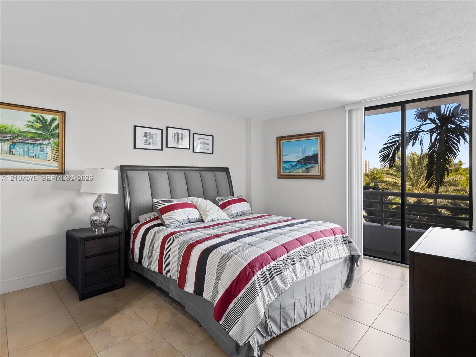 Neutral-toned tile flooring, large sliding glass door with access to a private balcony, and palm tree scenery
