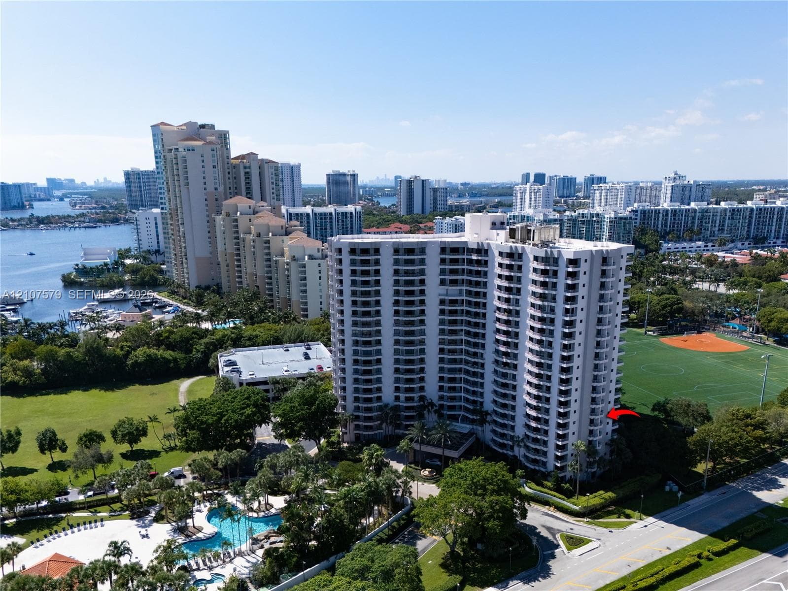 High-rise residential building featuring expansive private balconies, swimming pool with deck, and proximity to adjacent recreational fields