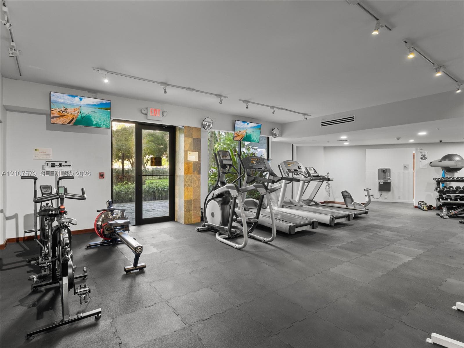 Fitness facility featuring rubberized flooring, track lighting, a stone-accented pillar, and a glass-paneled exterior door