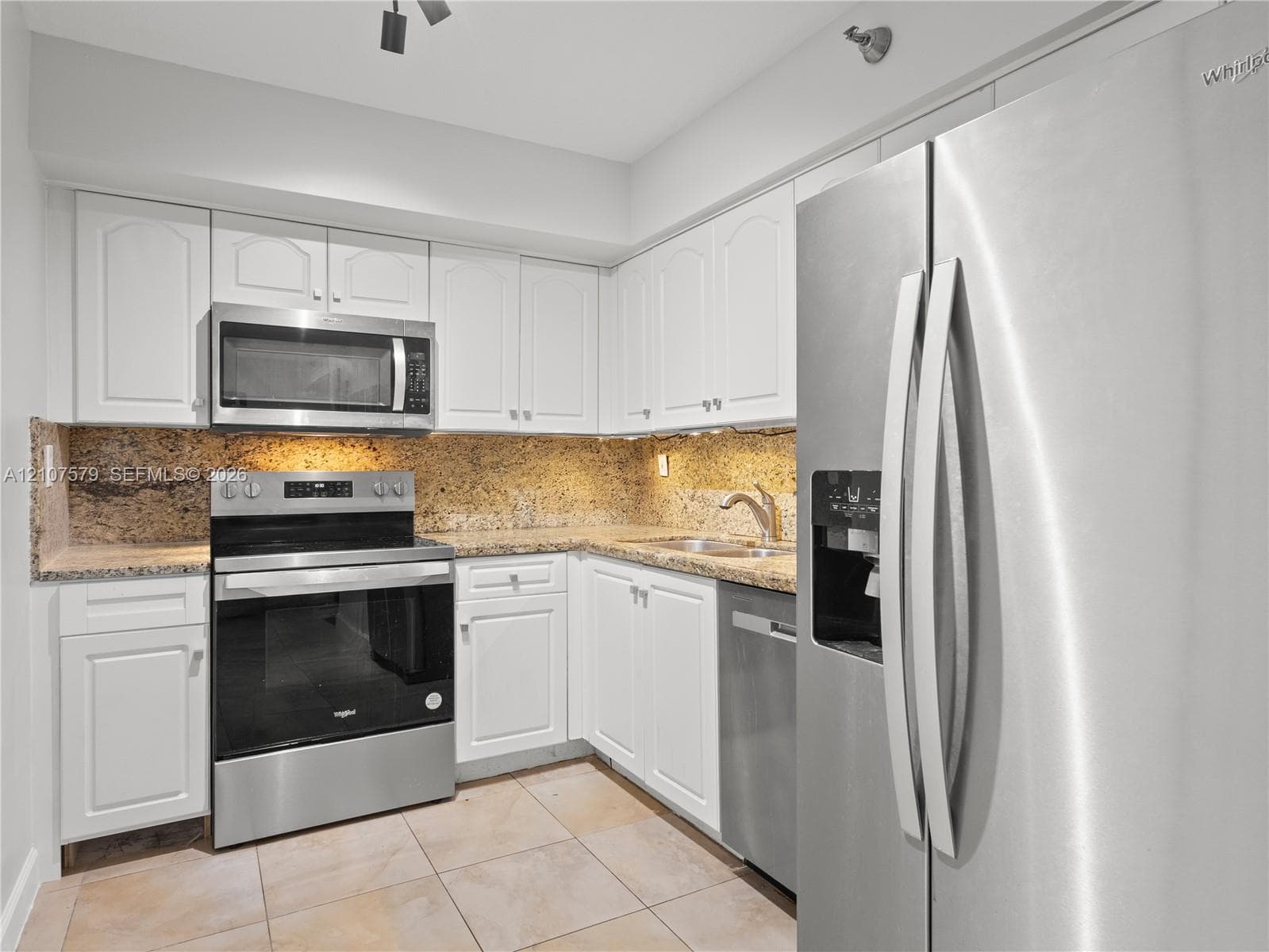 Kitchen featuring white cabinetry, stone countertops, tiled flooring, and stainless steel appliances including a refrigerator, dishwasher, range, and built-in microwave