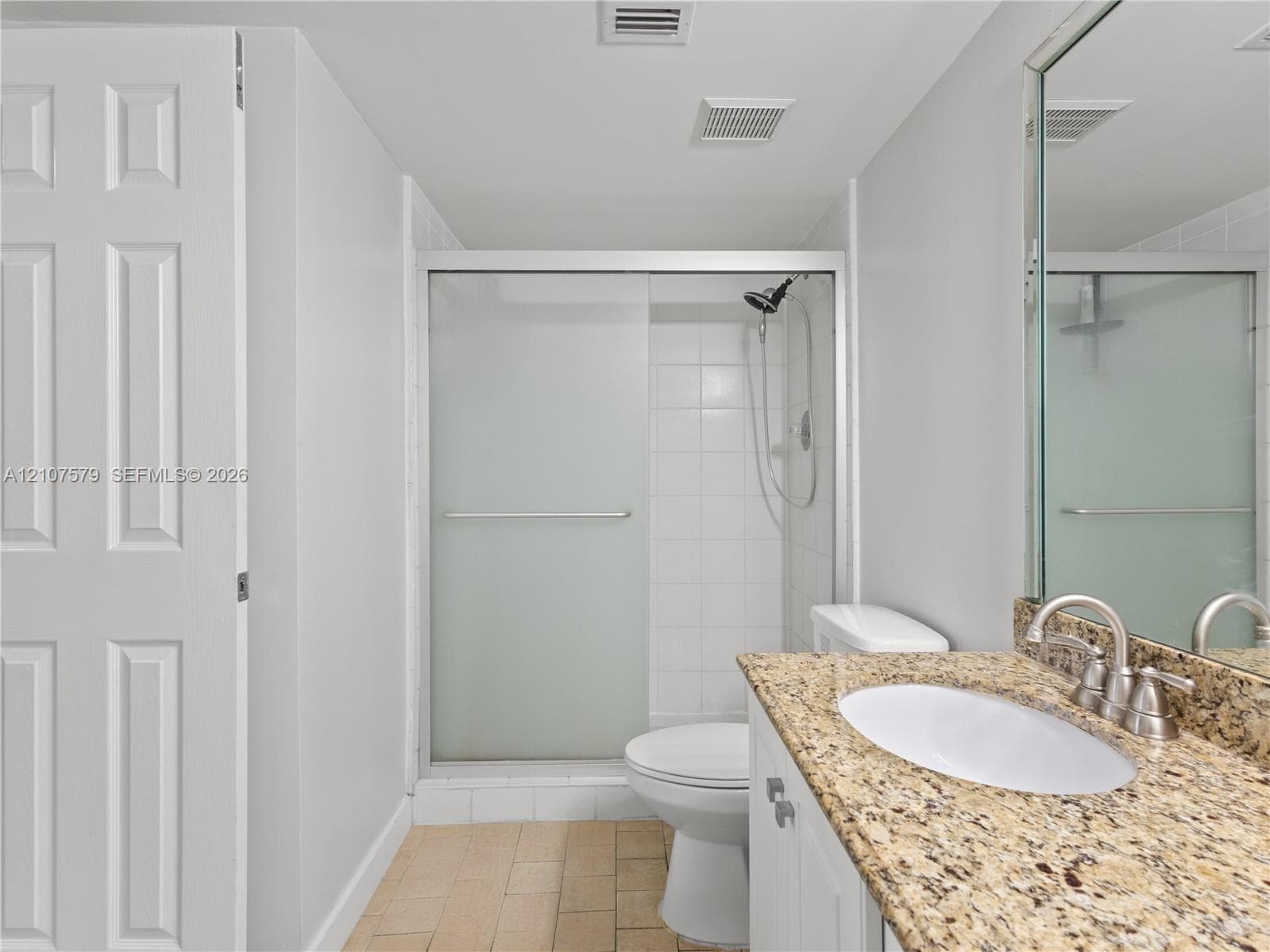 Bathroom featuring stone-finish countertop with an undermount oval sink, sliding glass shower enclosure, white cabinetry, and tile flooring