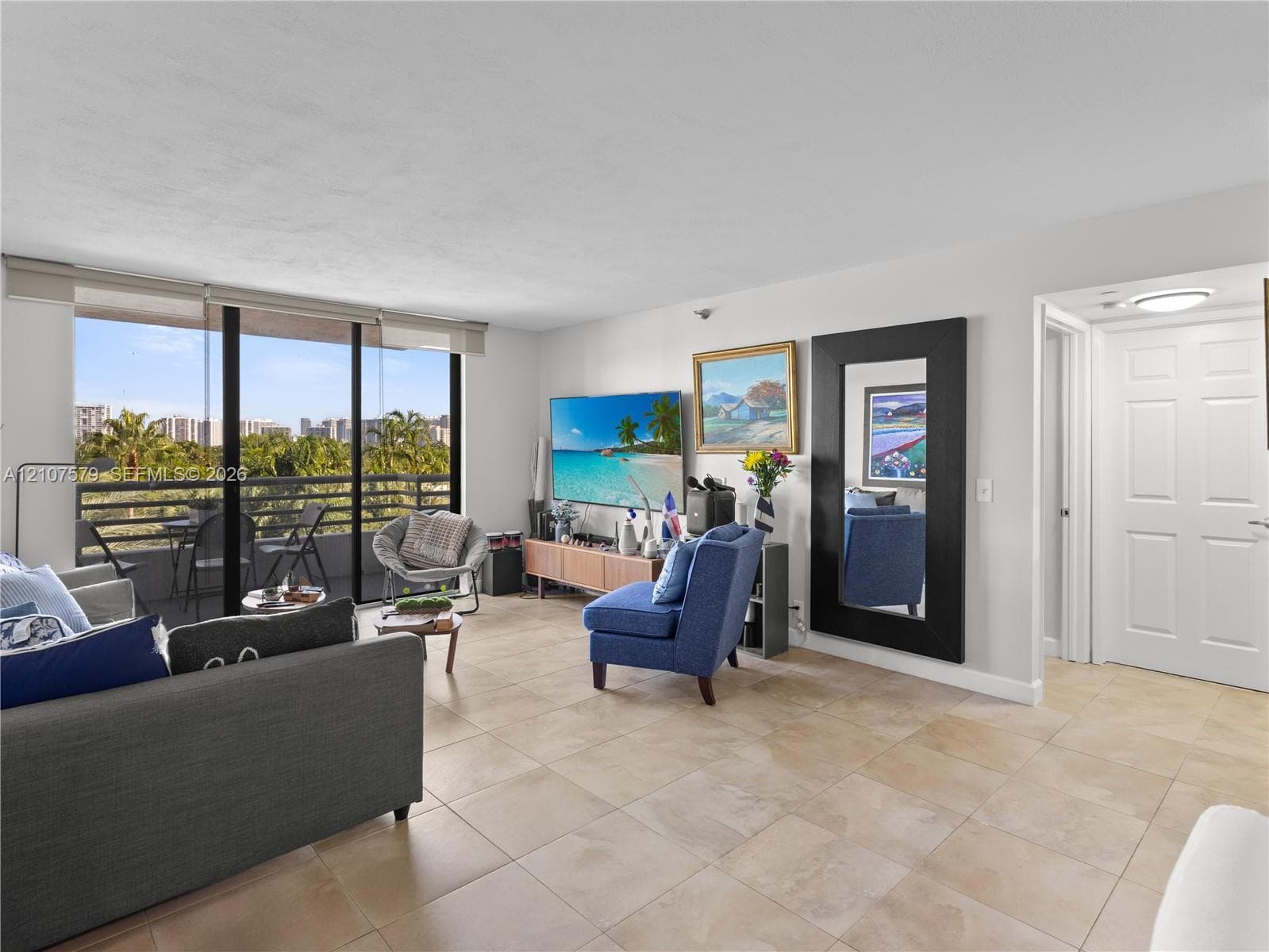 Open-concept interior featuring large-format ceramic tile flooring, sliding glass door access to a covered balcony, and a multi-panel door