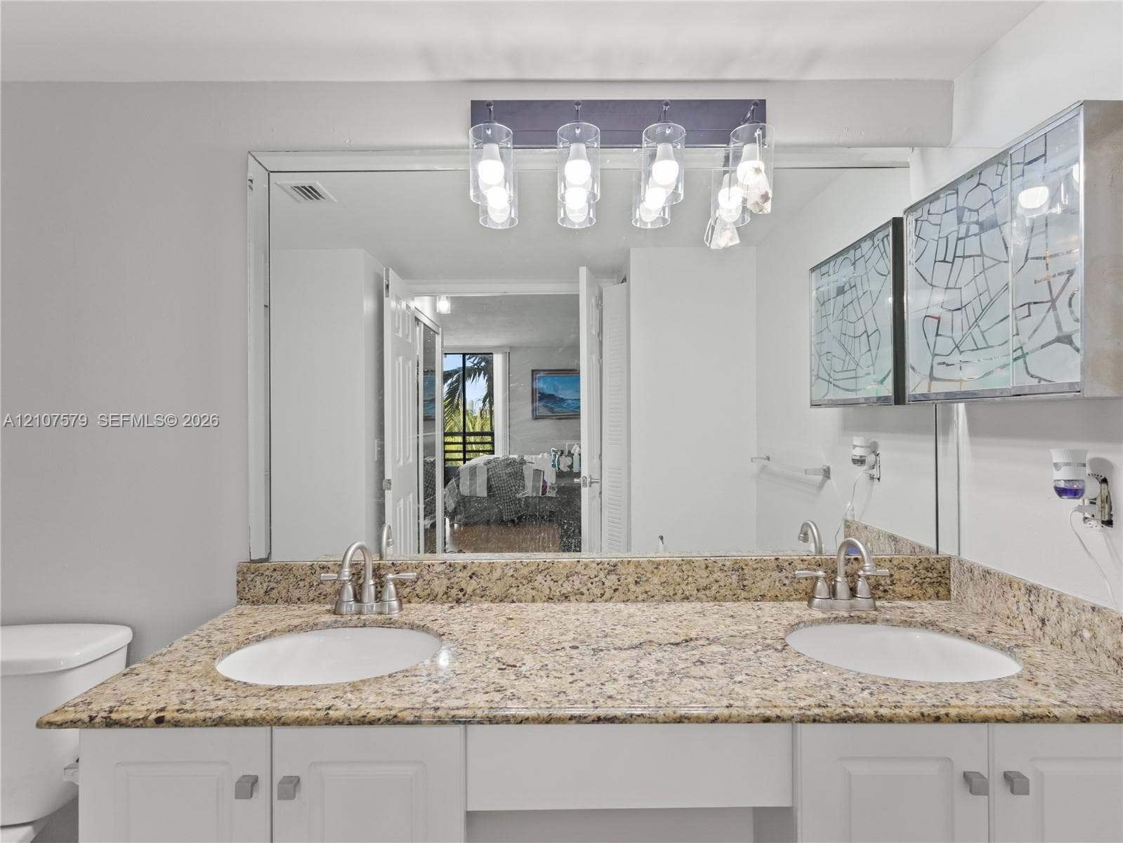 Dual-sink vanity with stone countertop, white cabinetry, large wall-mounted mirror, and multi-bulb decorative light fixture
