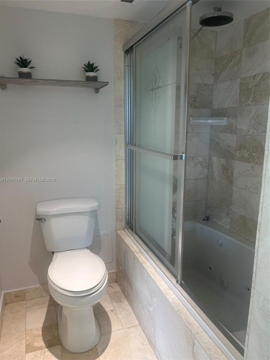 Tiled flooring with a built-in jetted tub, wall-mounted showerhead, and sliding glass shower enclosure