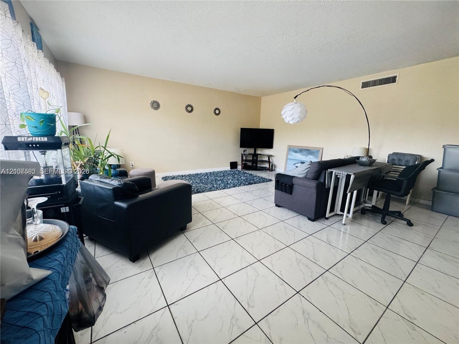 Large living area featuring neutral wall paint and white tile flooring with stone-patterned veining