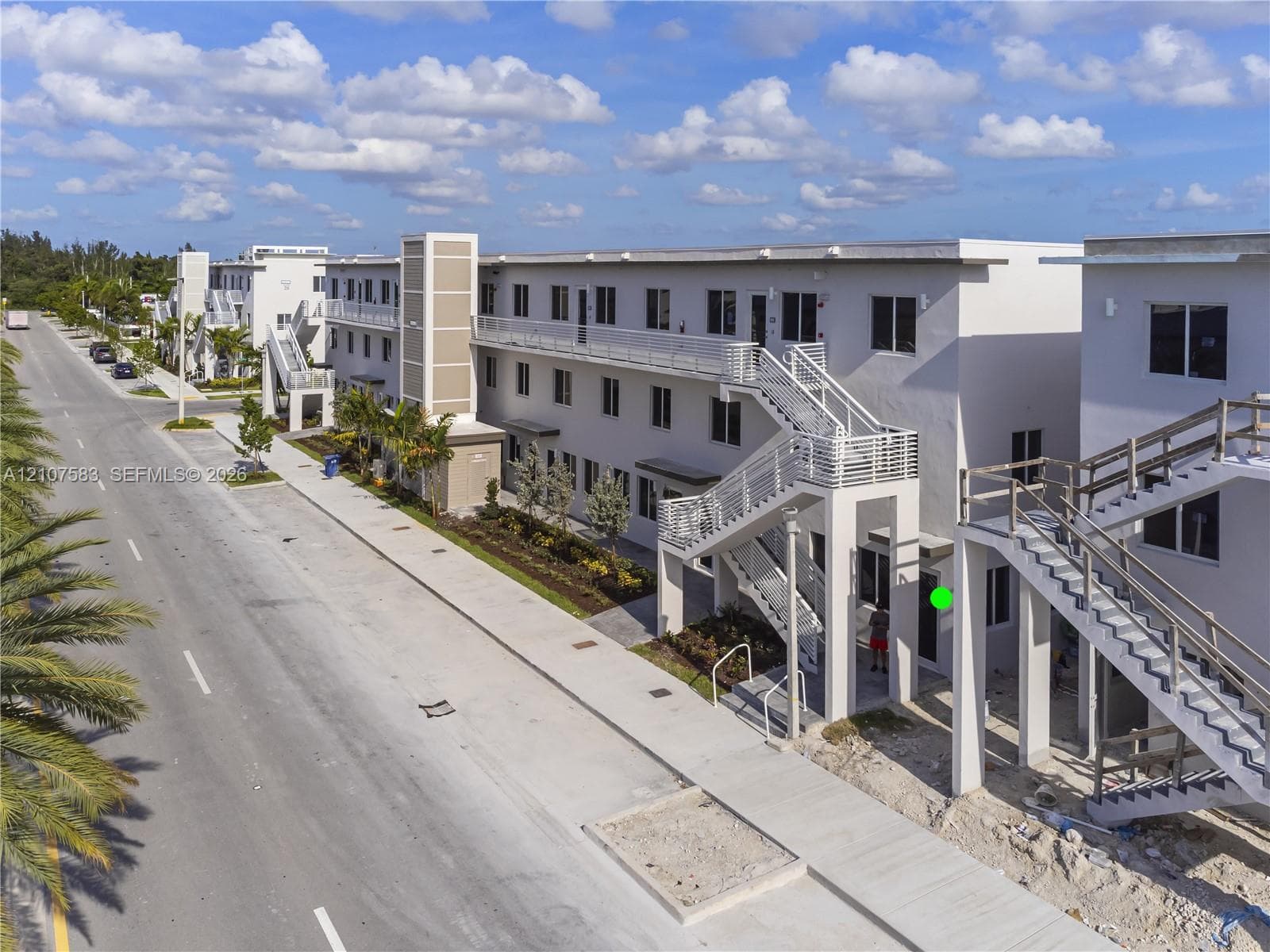 Multi-story exterior featuring light-toned stucco siding, metal staircases, exterior walkways with horizontal railings, and integrated wall-mounted lighting