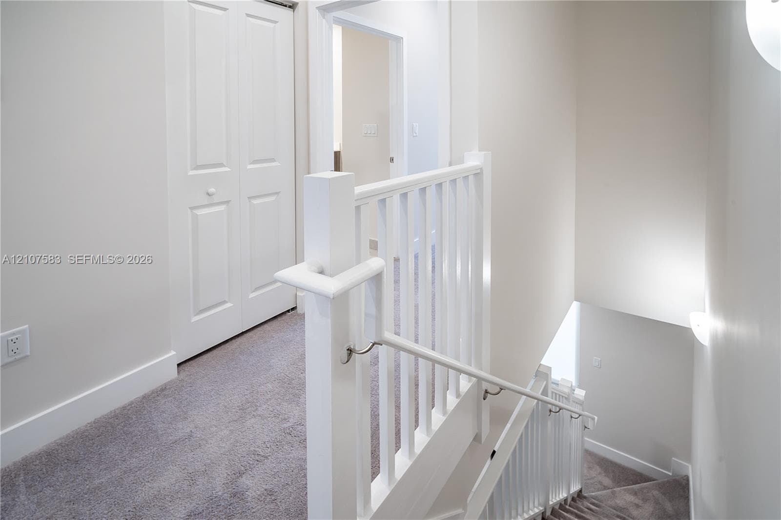 Staircase featuring a white wooden balustrade and handrail, carpeted flooring, and a multi-panel door