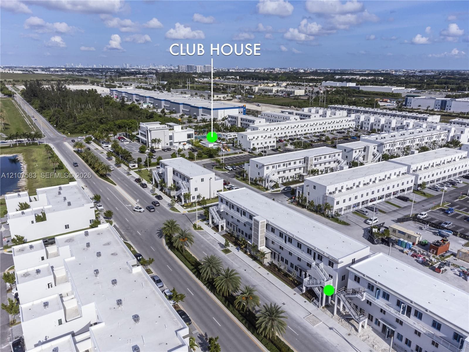 Aerial perspective of a multi-unit residential development featuring a dedicated clubhouse, paved parking areas, and mature palm landscaping