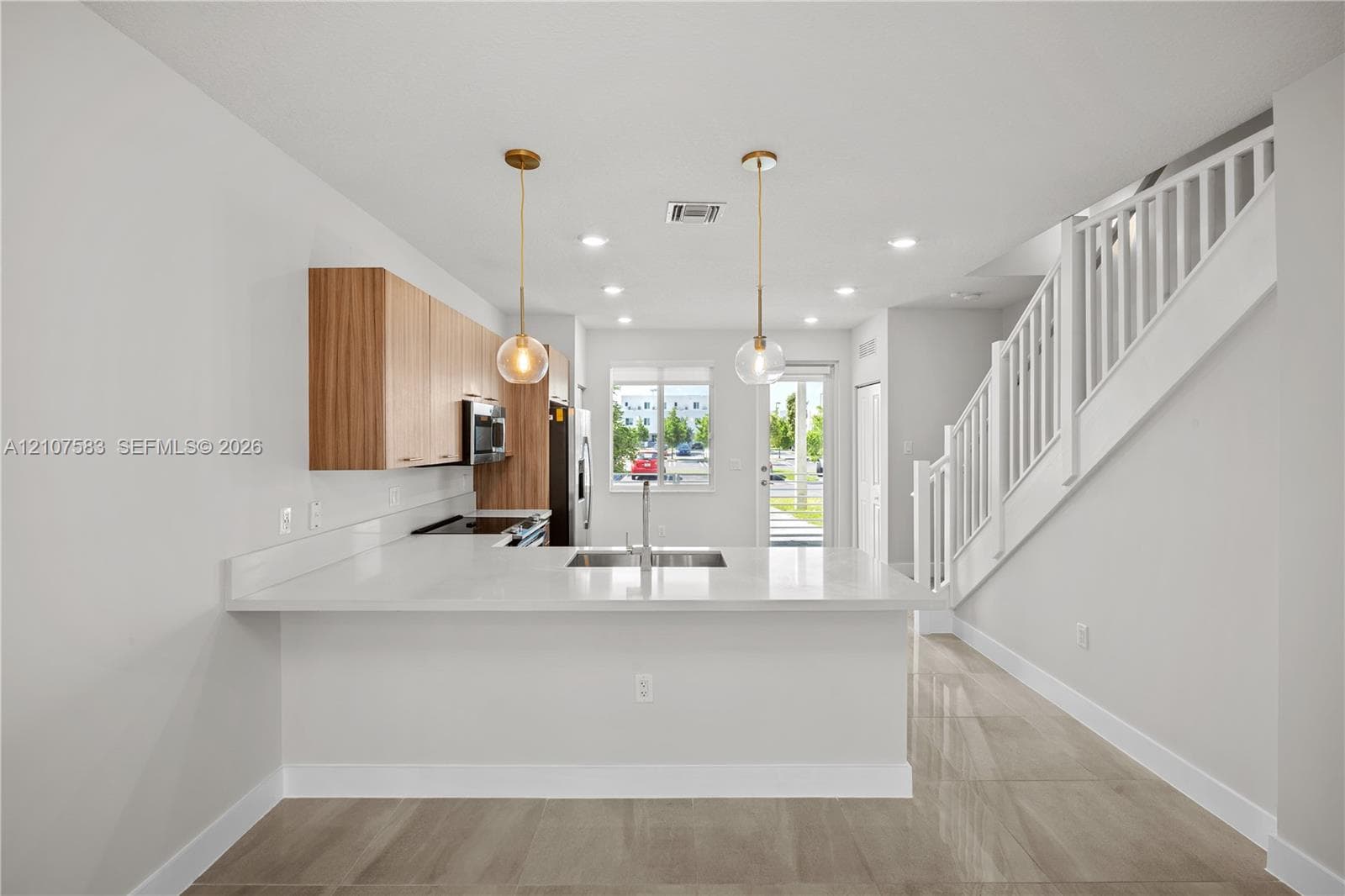 Kitchen featuring wood-finish cabinetry, quartz countertops, an undermount sink, pendant lighting, and polished tile flooring