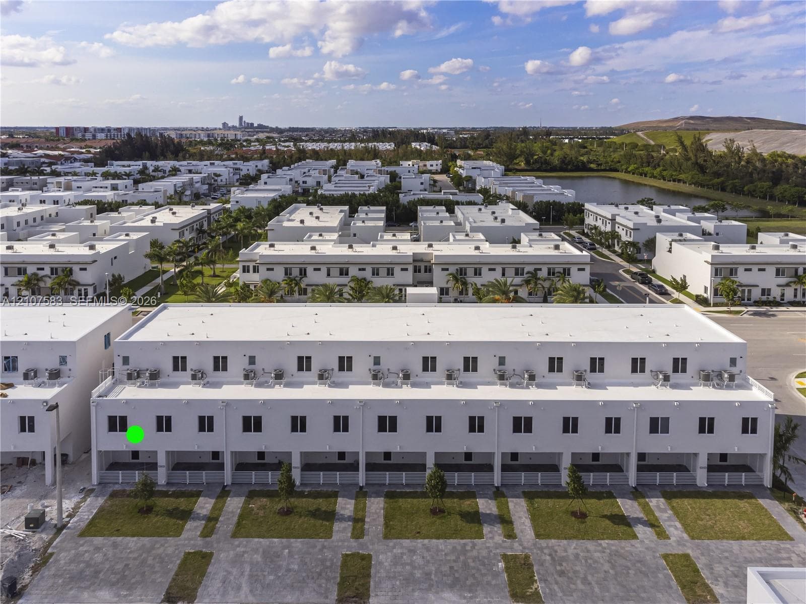 Multi-story townhouse exterior featuring a white stucco facade, flat roofline, paved ground-level patios, and dedicated lawn segments