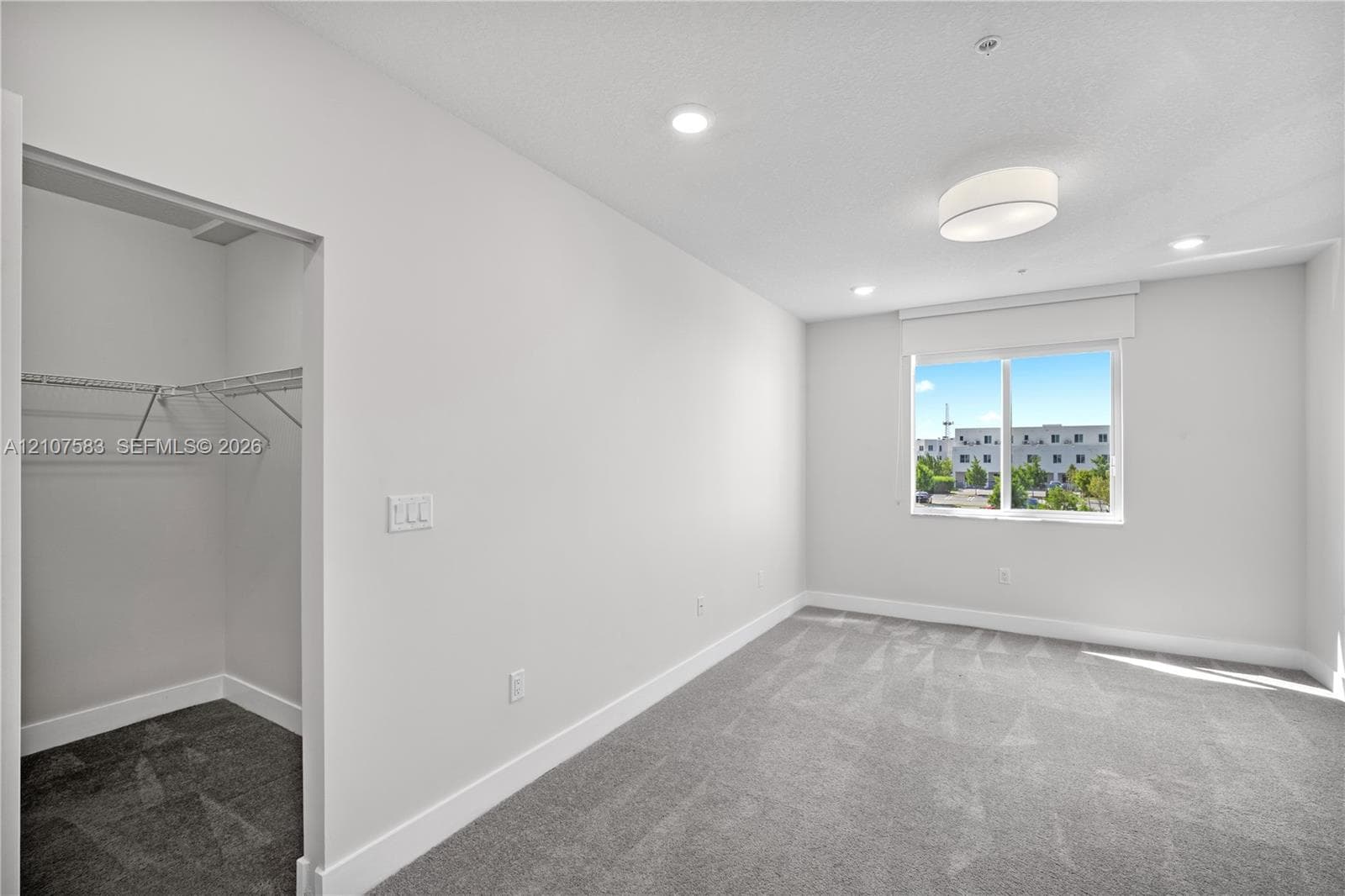 Neutral-toned room featuring wall-to-wall carpeting, recessed lighting, a ceiling-mounted light fixture, and a built-in closet with wire shelving