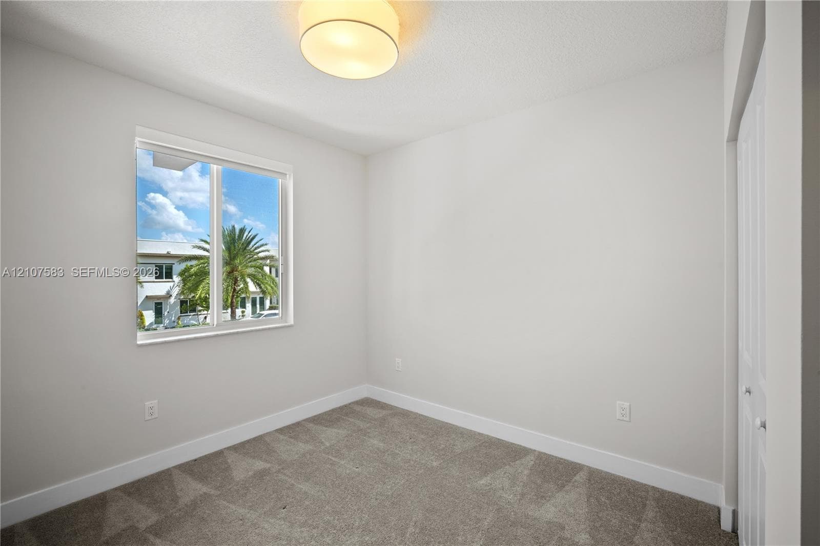 Neutral-toned interior space featuring neutral wall-to-wall carpeting, a single-pane sliding window, a circular flush-mount ceiling light fixture, and a built-in closet with double-panel doors