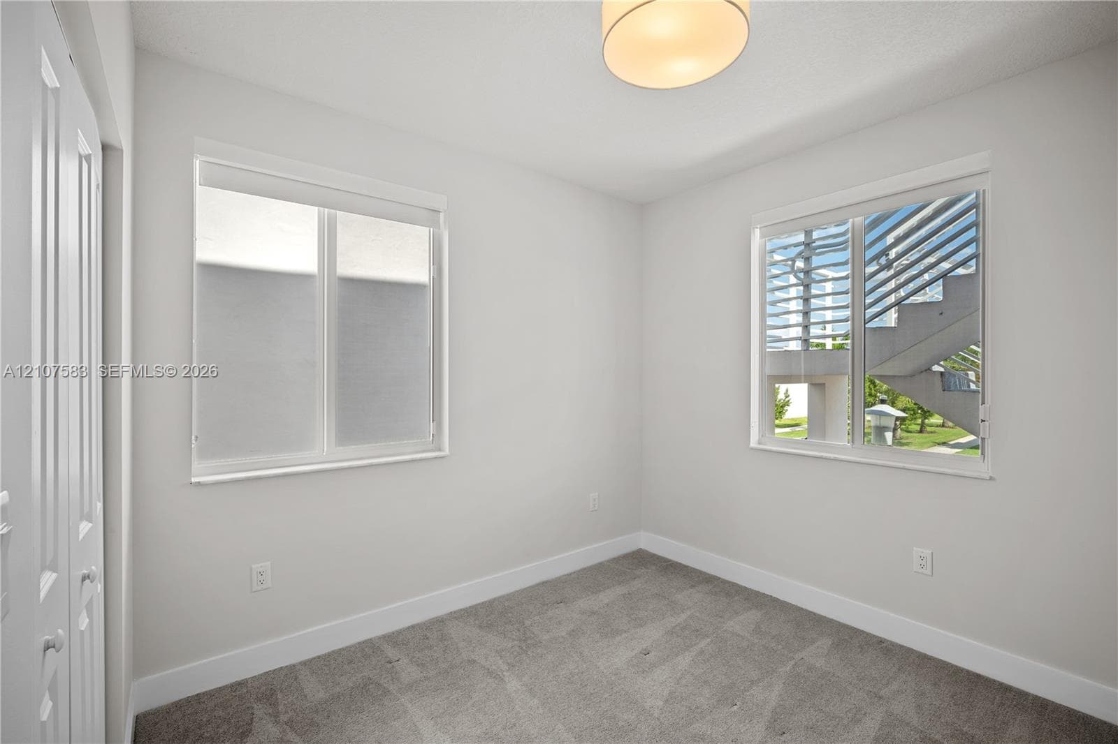 Neutral-toned interior featuring wall-to-wall carpeting, dual windows, a flush-mount drum ceiling light, and double-door closet storage