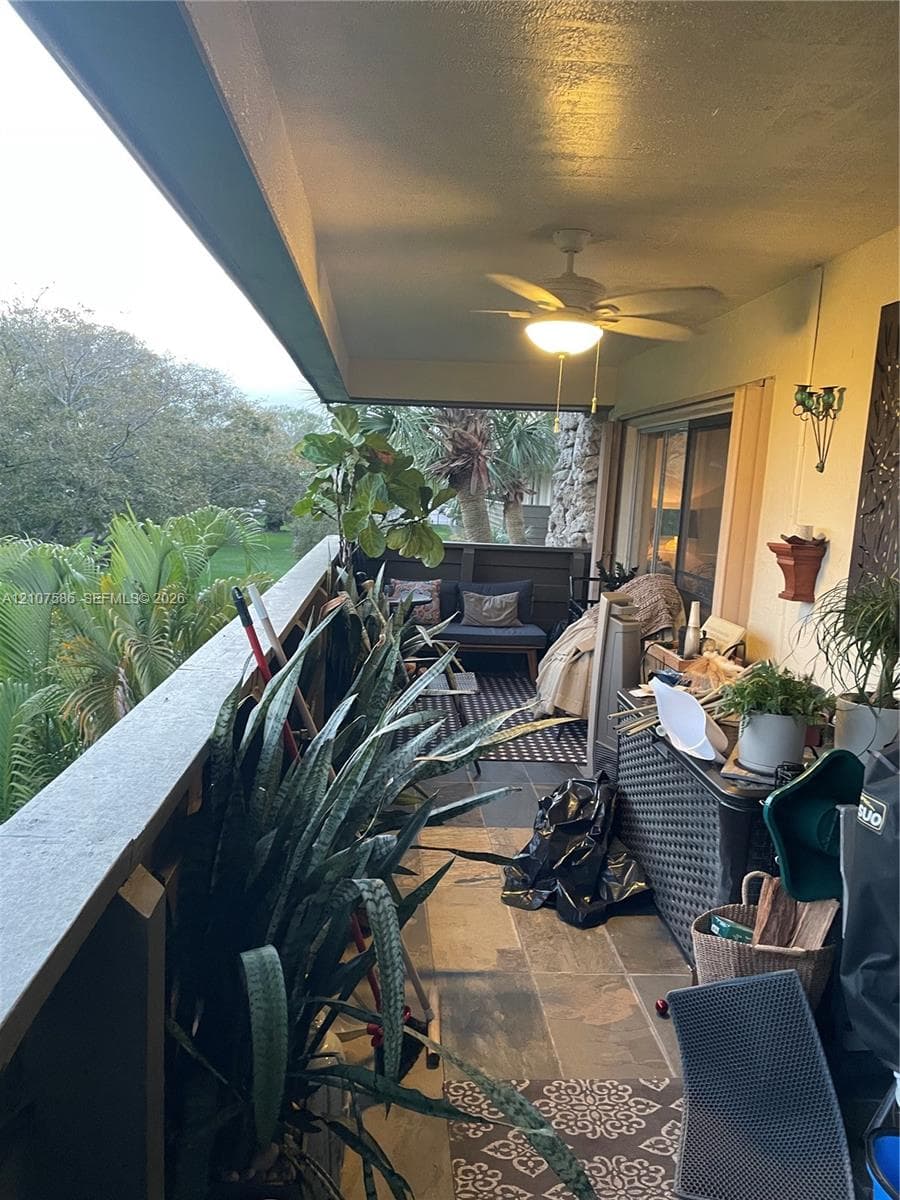 Covered balcony featuring stone-tile flooring, ceiling-mounted lighting with integrated fan, and solid wood-panel railing