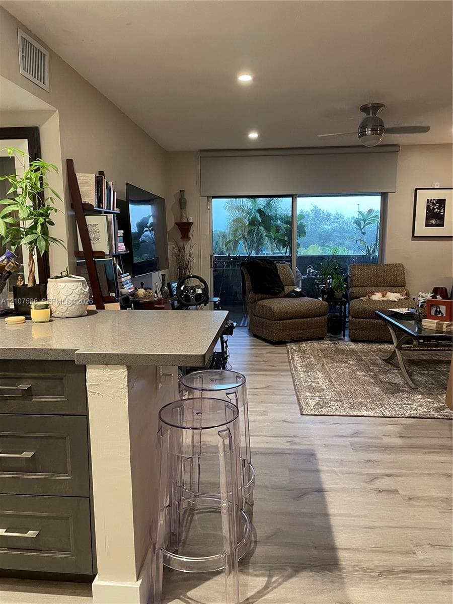 Kitchen island with a solid surface countertop, gray cabinetry, wood-finish flooring, recessed ceiling lighting, and sliding glass doors