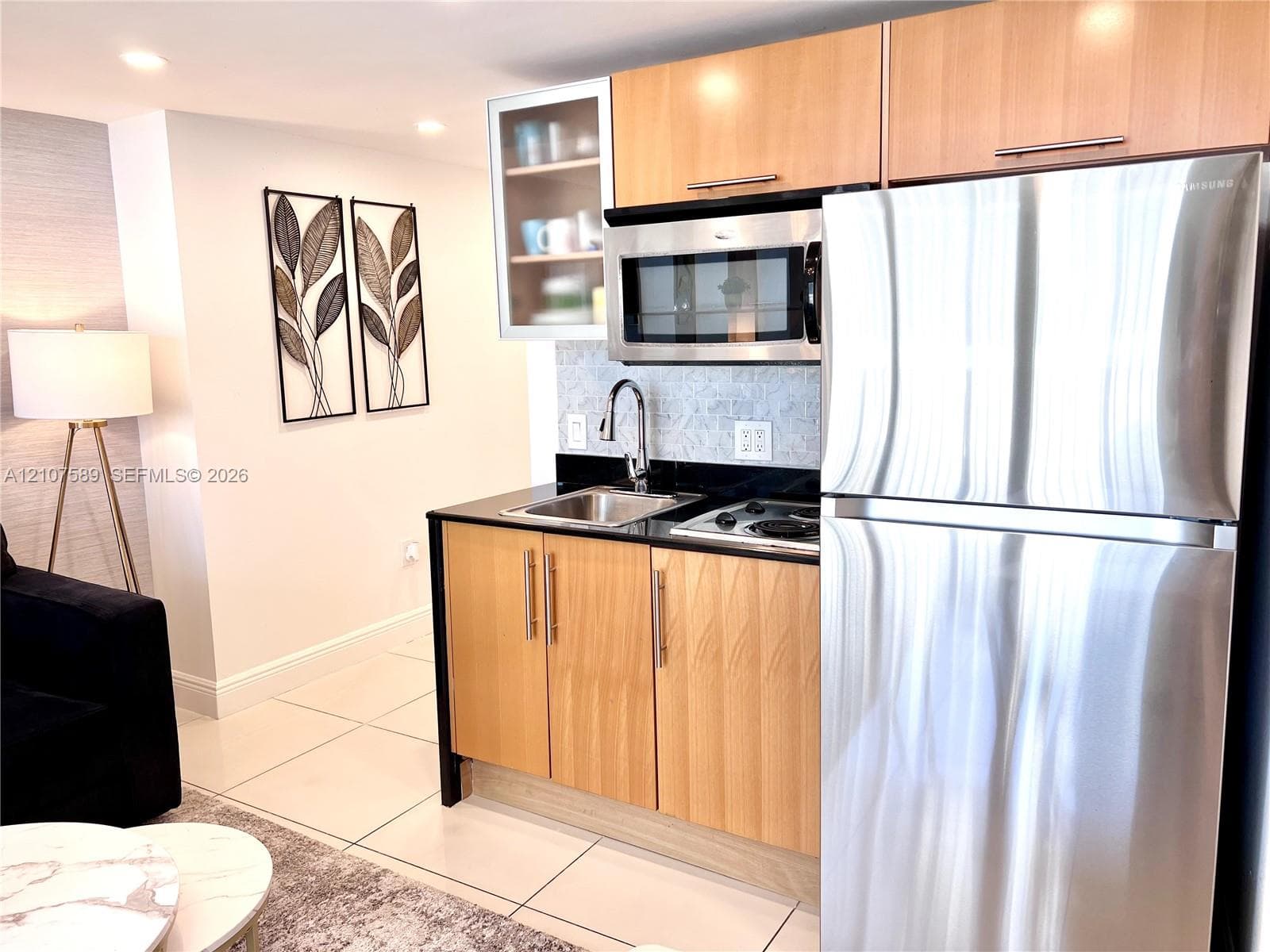 Kitchenette featuring light wood cabinetry, stone countertops, stainless steel refrigerator, built-in microwave, and arched faucet