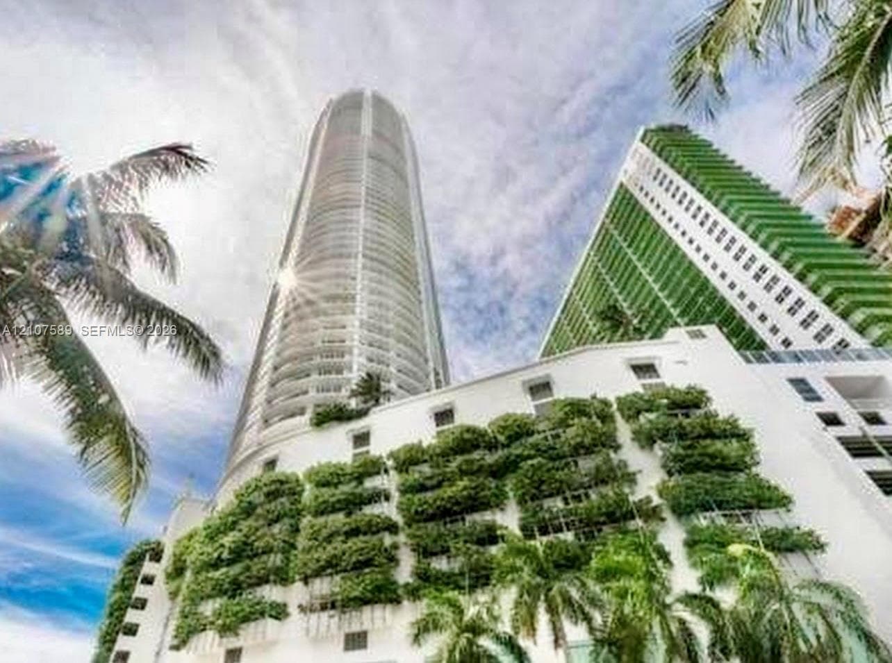 High-rise architectural structure featuring a cylindrical glass facade, exterior vertical garden greenery, and private wrap-around balconies