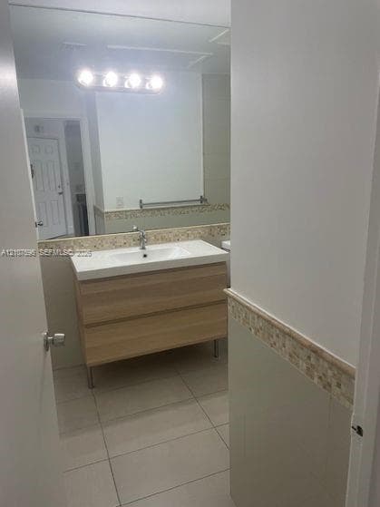 Modern vanity with a rectangular sink, light wood-finish cabinetry, ceramic tile flooring, and a decorative mosaic tile backsplash