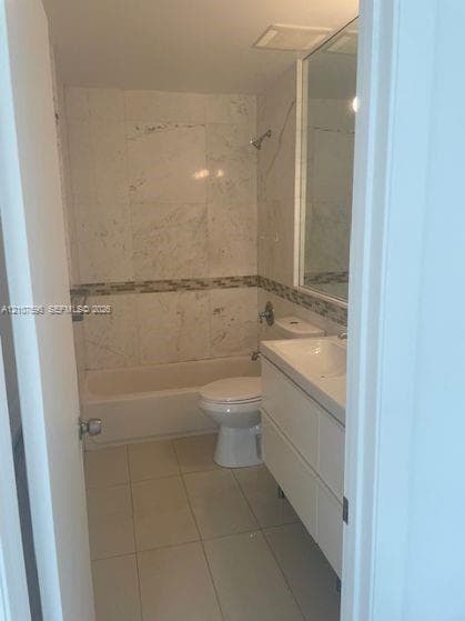 Full bathroom featuring a tub-shower combination with floor-to-ceiling stone tile surround, decorative mosaic accent border, white wall-mounted vanity, and large integrated mirror