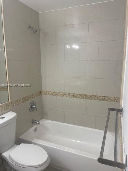 Full-size bathtub with shower combination, large-format neutral wall tile, decorative stone mosaic tile accent border, wall-mounted metal towel rack, and polished chrome fixtures