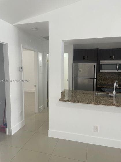 Kitchen featuring dark cabinetry, stone-surface countertops, stainless steel appliances, and tile flooring