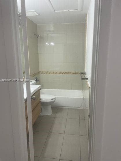 Full bathroom featuring a tub-shower combination with tile surround, wood-finish vanity, large-format floor tile, and wall-mounted hardware