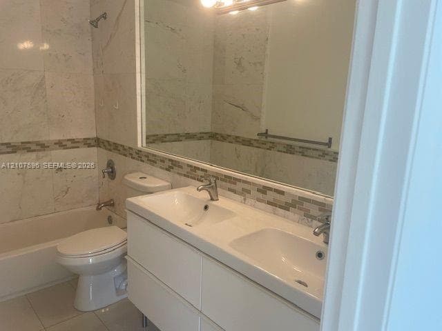 Bathroom featuring a dual-sink vanity with a white countertop, large wall-mounted mirror, mosaic tile backsplash, and a tiled shower-tub combination