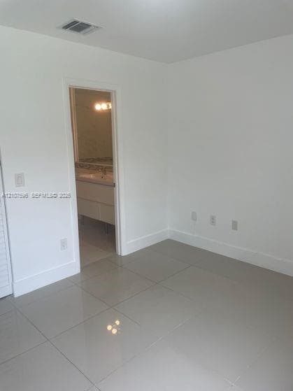 Neutral interior space featuring polished tile flooring, crisp white walls, and a recessed doorway leading to a vanity area with a stone-top counter