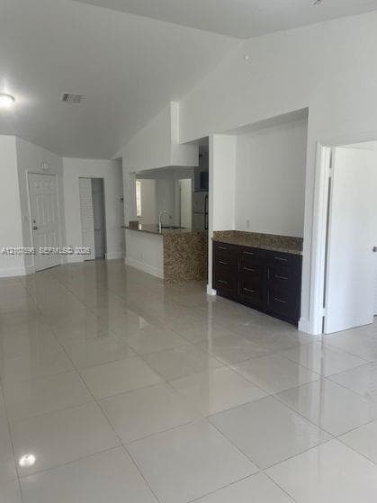 Open-concept interior featuring high ceilings, polished tile flooring, dark cabinetry with stone countertops, and a breakfast bar