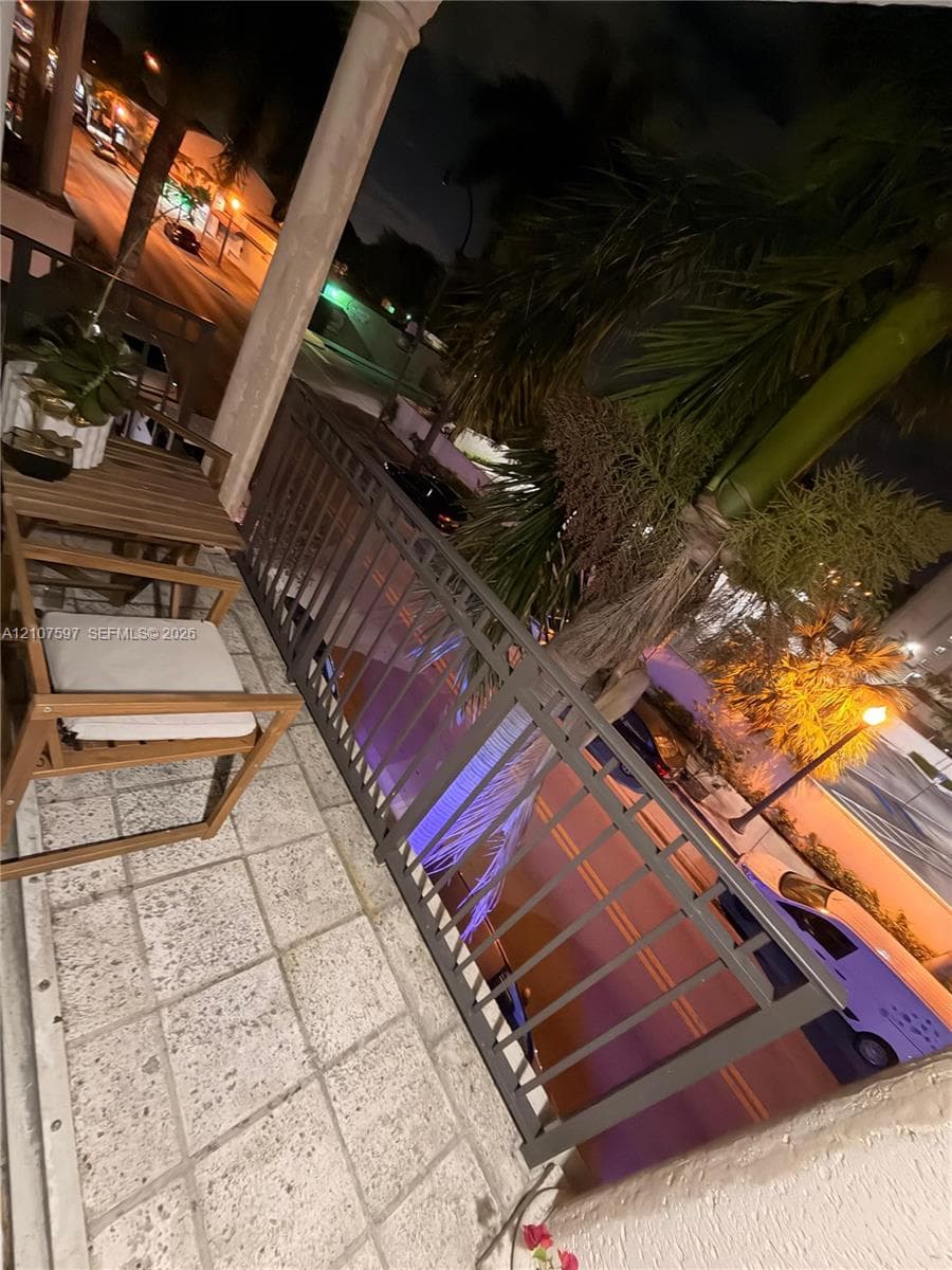 Balcony featuring stone-tile flooring, decorative metal railing, and a columned support structure